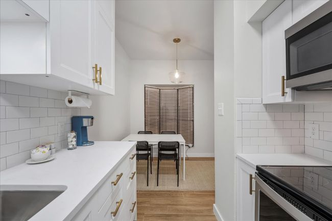 Kitchen with appliances with stainless steel finishes, light wood-style flooring, backsplash, light countertops, and white cabinetry | Image 17