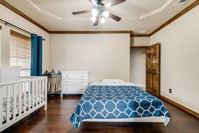 Bedroom featuring a tray ceiling, hardwood / wood-style flooring, crown molding, ceiling fan, and baseboards | Image 6