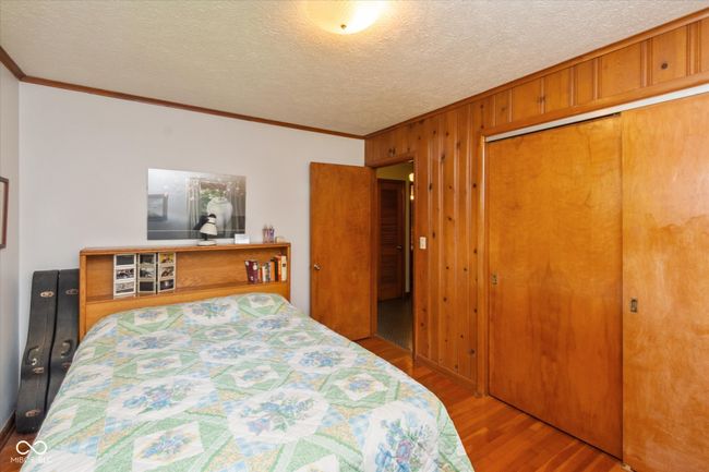 bedroom with ornamental molding, wood finished floors, wood walls, a closet, and a textured ceiling | Image 18
