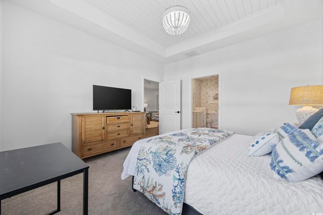 Carpeted bedroom with an inviting chandelier, wooden ceiling, a raised ceiling, connected bathroom, and visible vents | Image 22