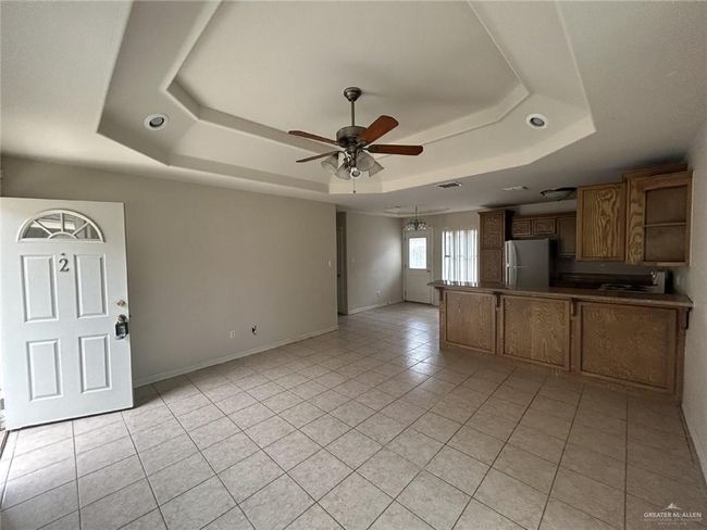 Unfurnished living room with a raised ceiling, ceiling fan, light tile patterned flooring, and baseboards | Image 12