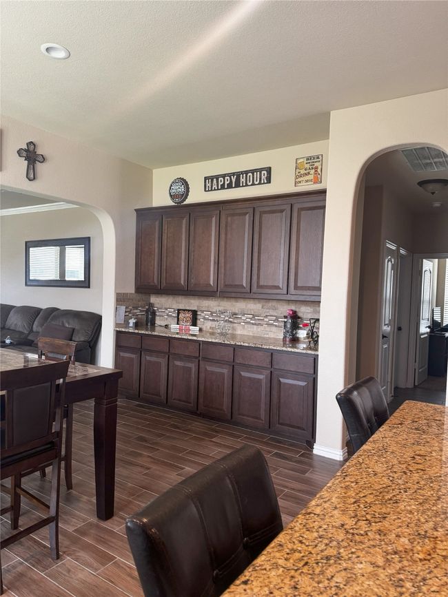 Kitchen with arched walkways, dark brown cabinetry, wood tiled floors, decorative backsplash, and light stone counters | Image 20