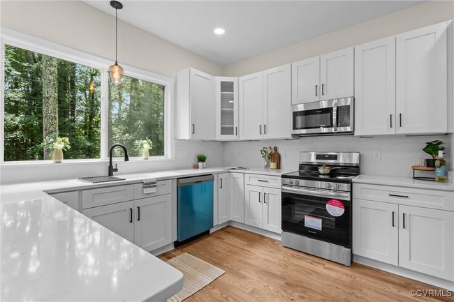 Kitchen featuring appliances with stainless steel finishes, white cabinetry, hanging light fixtures, glass insert cabinets, and light wood-style flooring | Image 14