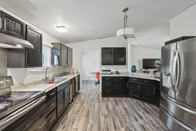 Kitchen with vaulted ceiling, a sink, hanging light fixtures, light wood-style flooring, and appliances with stainless steel finishes | Image 7