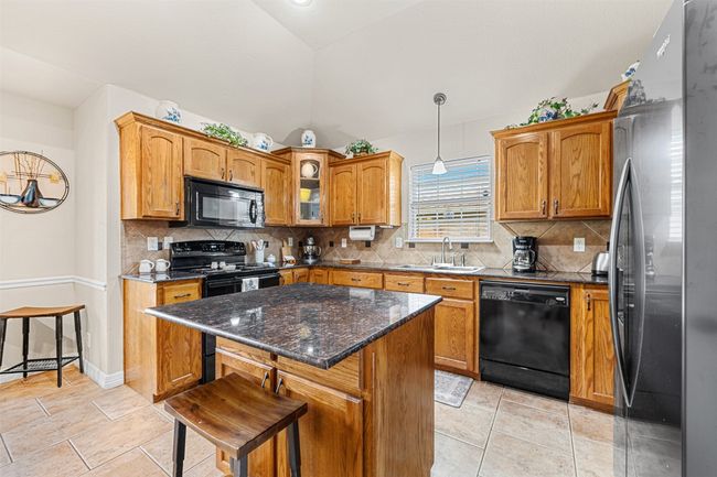 Kitchen with black appliances, a sink, brown cabinetry, a kitchen island, and backsplash | Image 14