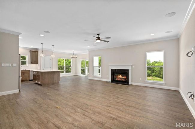 Unfurnished living room featuring crown molding, a fireplace, a ceiling fan, wood finished floors, and baseboards | Image 9