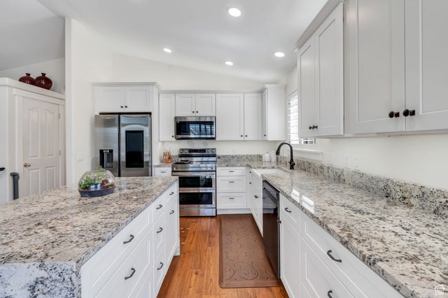 Kitchen with appliances with stainless steel finishes, vaulted ceiling, white cabinetry, light stone counters, and recessed lighting | Image 6