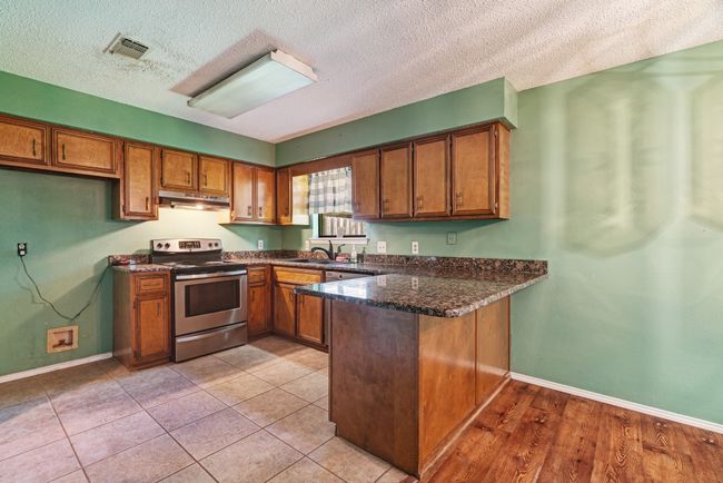Kitchen with stainless steel electric stove, under cabinet range hood, a peninsula, brown cabinets, and a textured ceiling | Image 4