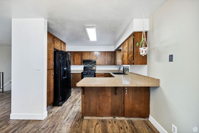 Kitchen with black appliances, a peninsula, baseboards, light countertops, and wood finished floors | Image 11