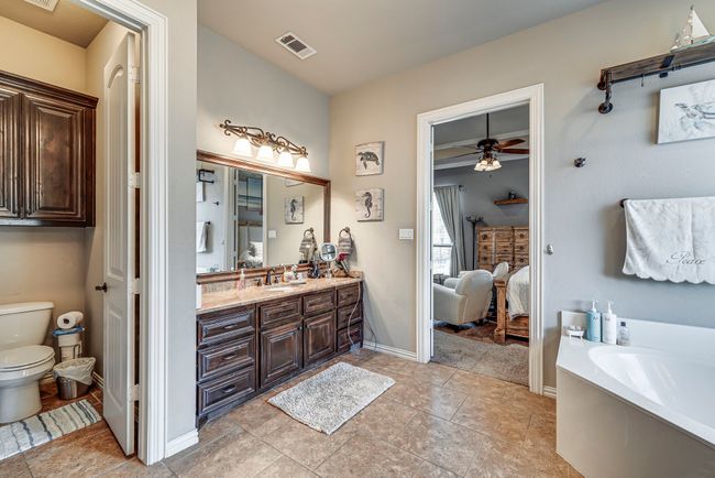 Primary bathroom featuring tile patterned floors, double vanity, ceiling fan, toilet, and a bathing tub | Image 5