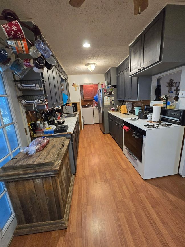 Kitchen with white gas stove, light wood-style floors, a textured ceiling, light countertops, and stove | Image 18