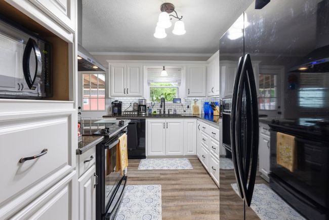 Kitchen with black appliances, plenty of natural light, crown molding, light wood finished floors, and white cabinetry | Image 6