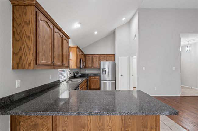 Kitchen with appliances with stainless steel finishes, brown cabinets, a peninsula, high vaulted ceiling, and recessed lighting | Image 25