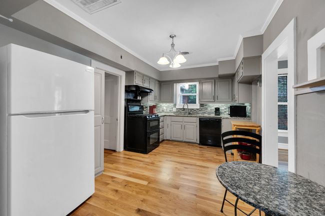 Kitchen featuring black appliances, a sink, ornamental molding, a chandelier, and under cabinet range hood | Image 9