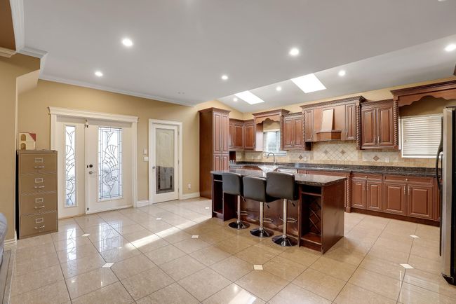 Kitchen featuring custom exhaust hood, a kitchen island with sink, a breakfast bar area, backsplash, and crown molding | Image 15