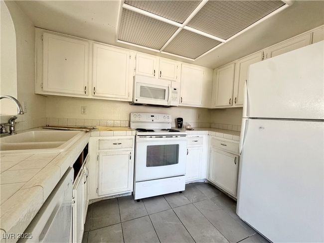 Kitchen with white appliances, a sink, tile counters, white cabinets, and light tile patterned flooring | Image 10