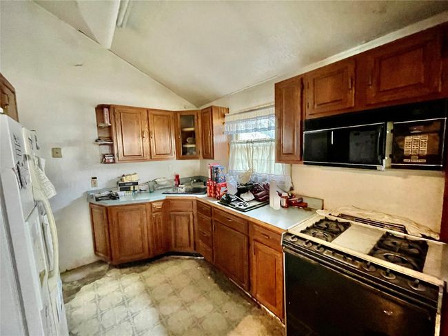 Kitchen with freestanding refrigerator, black microwave, brown cabinetry, gas range, and light countertops | Image 4