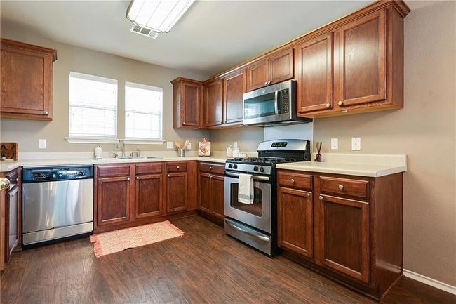 Kitchen featuring stainless steel appliances, a sink, dark wood-style floors, and light countertops | Image 5
