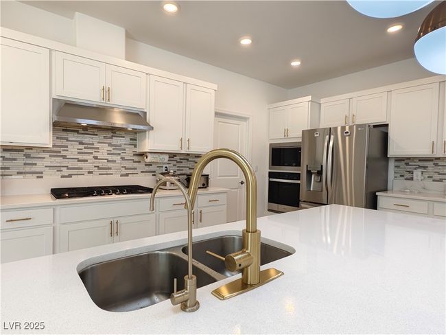Kitchen with white cabinetry, a sink, appliances with stainless steel finishes, light countertops, and under cabinet range hood | Image 16