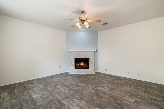 Unfurnished living room featuring dark wood-style flooring, a stone fireplace, a ceiling fan, baseboards, and visible vents | Image 20