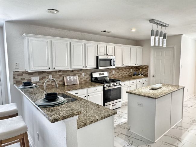 Kitchen featuring appliances with stainless steel finishes, light marble finish floors, white cabinetry, tasteful backsplash, and recessed lighting | Image 8