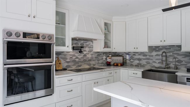 Kitchen featuring double oven, black electric cooktop, premium range hood, white cabinetry, and backsplash | Image 12