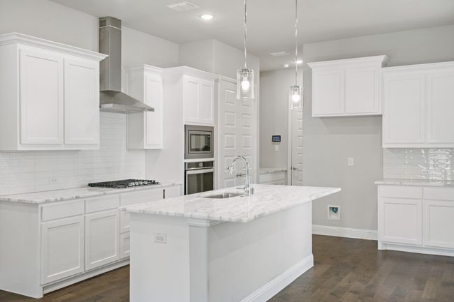 Kitchen with wall chimney range hood, white cabinets, a sink, and stainless steel appliances | Image 13