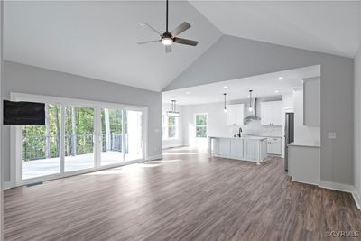 Unfurnished living room with plenty of natural light, ceiling fan with notable chandelier, hardwood / wood-style floors, and high vaulted ceiling | Image 3