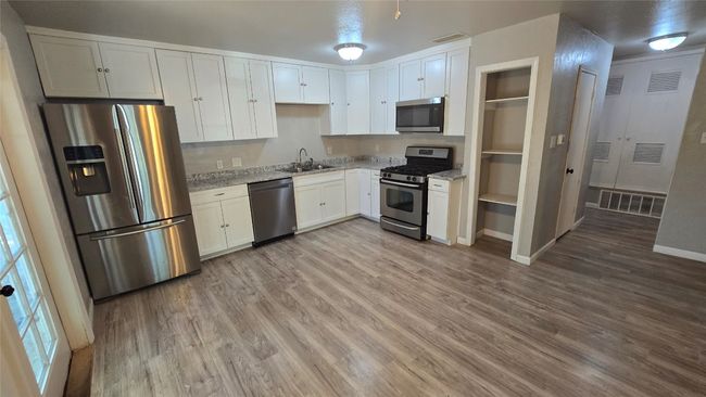 Kitchen with appliances with stainless steel finishes, light wood-style floors, light stone counters, and white cabinetry | Image 6