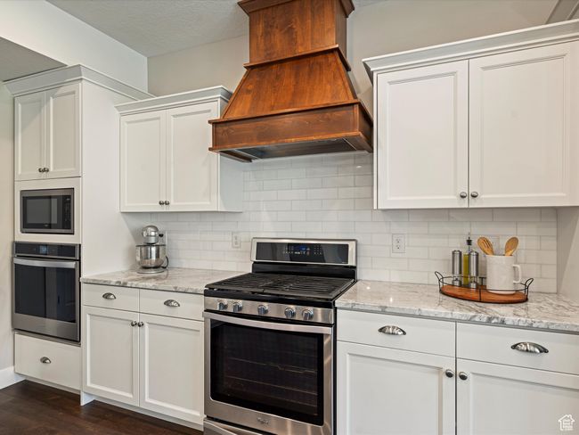 Kitchen with appliances with stainless steel finishes, custom range hood, white cabinetry, dark wood-style floors, and decorative backsplash | Image 10