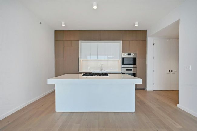 A streamlined culinary space highlighted by Bosch appliances, a gas cooktop built into the expansive quartz island, and custom cabinetry that seamlessly conceals the refrigerator and dishwasher for a clean, modern aesthetic. | Image 4