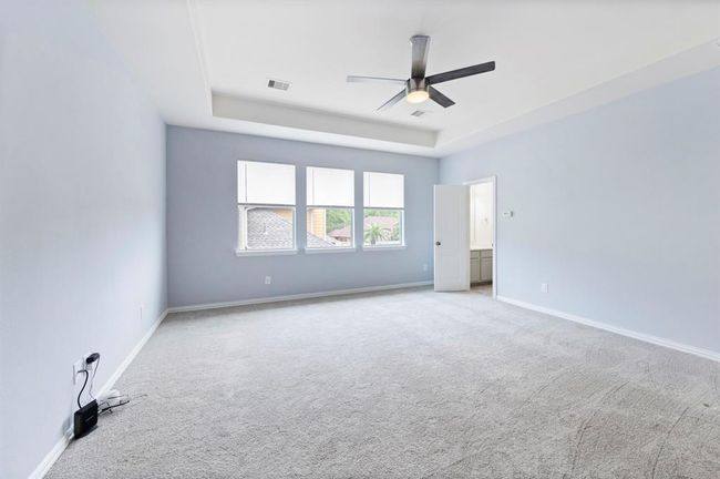 Bright and airy upstairs game room with plush carpet, tray ceiling, sleek fan, and triple windows for abundant natural light—complete with a half bathroom. | Image 19