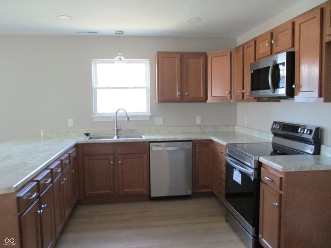 kitchen featuring brown cabinets, appliances with stainless steel finishes, light countertops, and a sink | Image 10