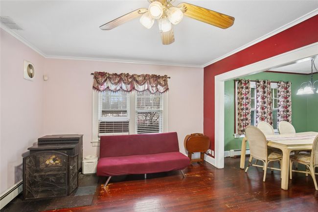 Sitting room with a wood stove, visible vents, a baseboard radiator, and hardwood / wood-style floors | Image 6