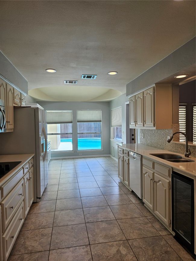 Kitchen with wine cooler, light countertops, tasteful backsplash, dishwasher, and tile patterned flooring | Image 5