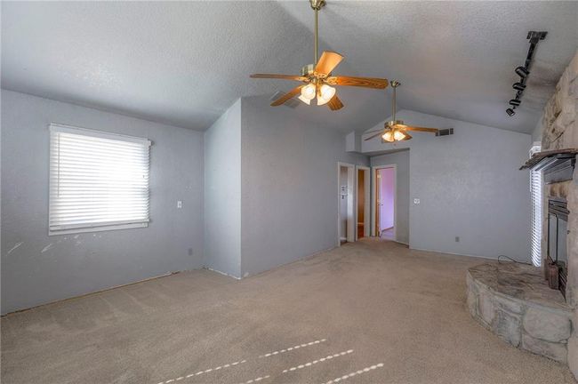 Unfurnished living room featuring vaulted ceiling, carpet flooring, a textured ceiling, a ceiling fan, and a fireplace | Image 18