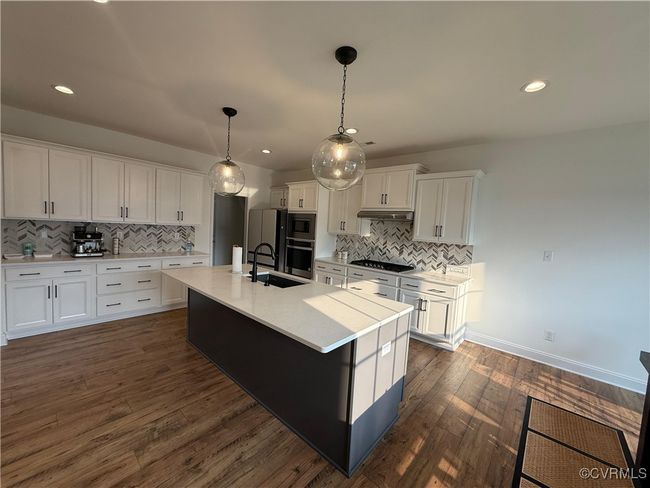 Kitchen featuring black stovetop, built in microwave, a sink, under cabinet range hood, and backsplash | Image 21