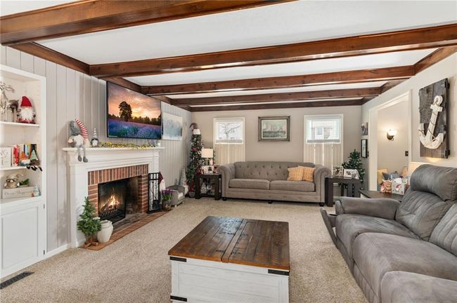 Carpeted living room featuring a brick fireplace and beam ceiling | Image 20
