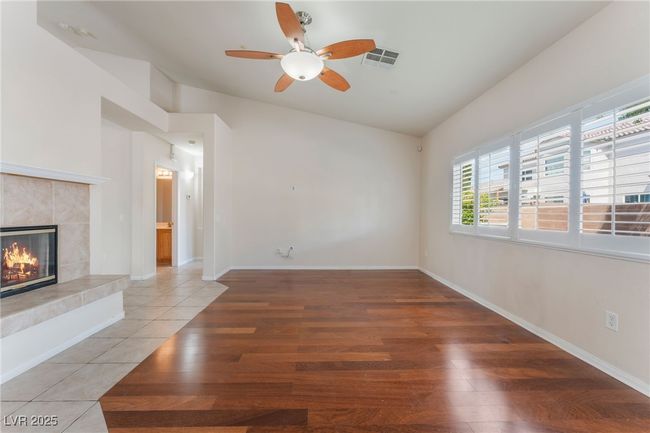 Unfurnished living room with a tiled fireplace, ceiling fan, light wood-style floors, vaulted ceiling, and baseboards | Image 10