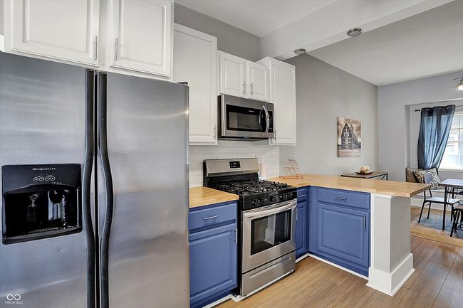 kitchen with a peninsula, light wood-type flooring, butcher block countertops, blue cabinetry, and appliances with stainless steel finishes | Image 18