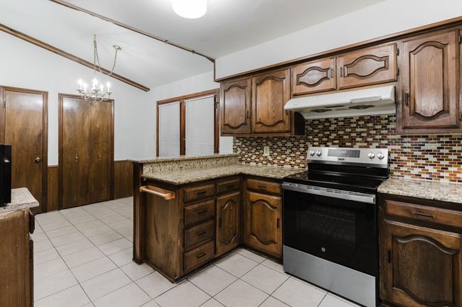 Kitchen with lofted ceiling, stainless steel range with electric stovetop, light tile patterned floors, under cabinet range hood, and a peninsula | Image 10
