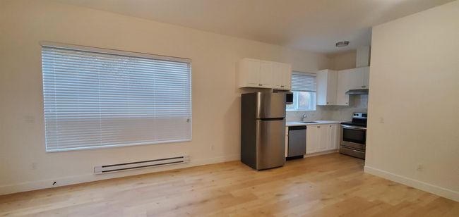 Kitchen featuring white cabinets, appliances with stainless steel finishes, a sink, light wood finished floors, and a baseboard heating unit | Image 33