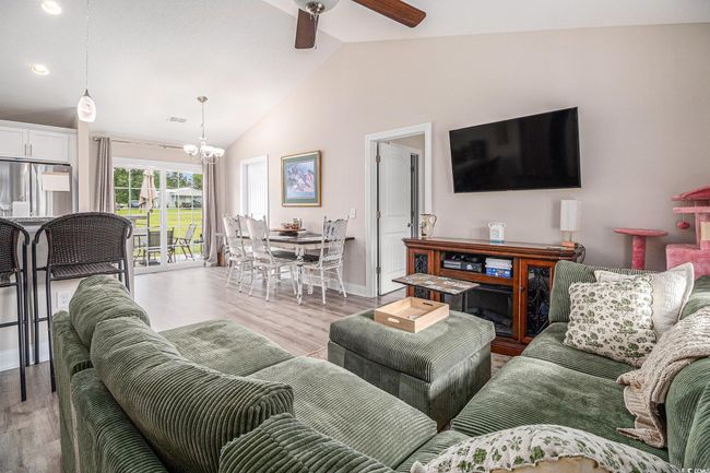 Living room with ceiling fan, light wood-type flooring, a chandelier, baseboards, and high vaulted ceiling | Image 4