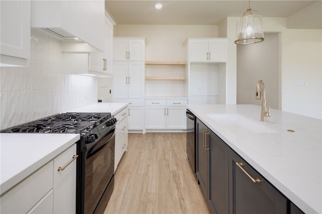 Kitchen featuring black gas stove, a sink, light wood finished floors, white cabinets, and dishwashing machine | Image 11