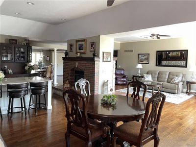 Dining area featuring a textured ceiling, vaulted ceiling, a brick fireplace, ceiling fan, and dark wood-type flooring | Image 3