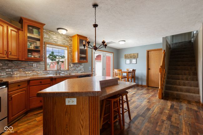 kitchen featuring a sink, dark wood finished floors, backsplash, a kitchen island, and a breakfast bar area | Image 9