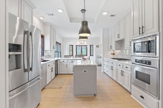 Kitchen with stainless steel appliances, a peninsula, backsplash, a tray ceiling, and light wood-style floors | Image 14