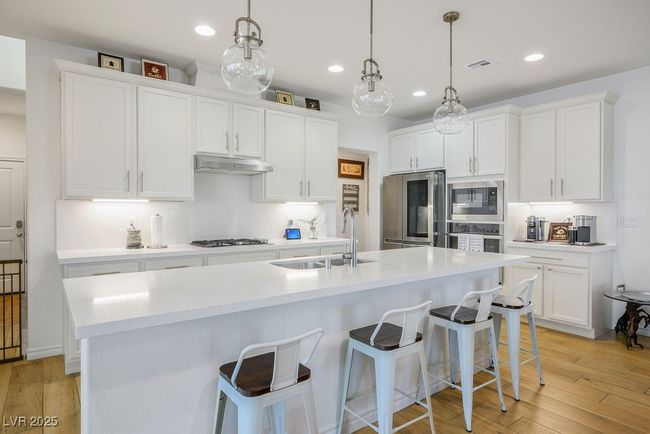 Kitchen with light wood finished floors, a sink, under cabinet range hood, white cabinets, and appliances with stainless steel finishes | Image 15