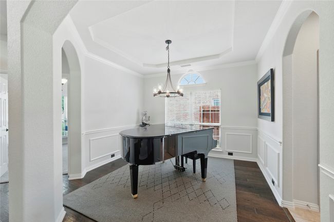 Dining area with a raised ceiling, dark wood finished floors, arched walkways, a wainscoted wall, and a chandelier | Image 8