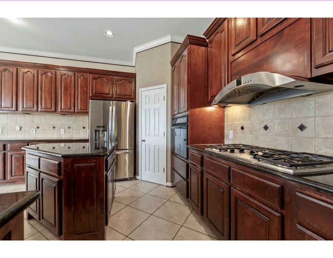 Kitchen featuring decorative backsplash, crown molding, stainless steel appliances, light tile patterned floors, and exhaust hood | Image 16